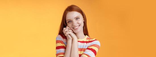 Romantic tender sensual attractive smiling redhead girlfriend melting heart feel warmth delighted lean palms grinning happily sweet gentle gift standing pleased orange background rejoicing thankful photo