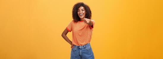 We hire you. Confident happy and awesome dark-skinned fashionable woman with curly hair holding hand on waist pointing at camera with index finger as if picking person or candidate, smiling photo