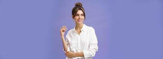 Feminine and stylish modern charming girl with gapped teeth and pimple posing in trendy white blouse and round earrings gazing left charmed and sensual with cute smile over purple background photo