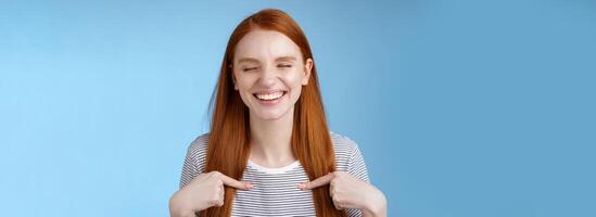 Happy cheerful glad young sportswoman redhead nominated smiling surprised laughing joyfully close eyes pointing herself chosen picked winning first prize, standing blue background photo