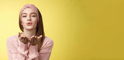 Happy valentines day. Charming romantic and sensual young flirty woman in knitted headband, sweater extending palms near folded lips sending air mwah, blowing kiss tender and gentle photo