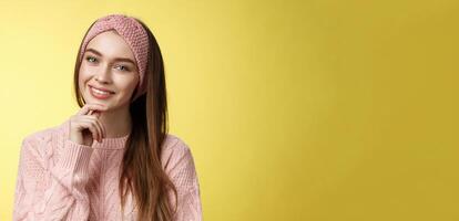 Happy young european woman in knitted headband, sweater tilting head touching chin and smiling silly, taking care of skin, feeling face glittering looking clear and healthy after skincare treatment photo