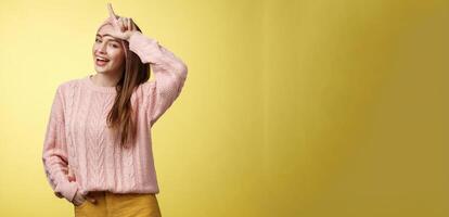 Attractive triumphing arrogant and confident cute glamourous woman in knitted sweater, headband showing l letter on forehead, loser sign and laughing over lost team, mocking having fun photo