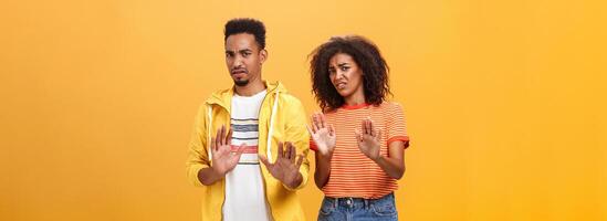 Two african american stylish friends hanging around interrupted by weird guy offering strange proposal shaking hands near chest in refusal and rejection gesture grimacing from aversion and dislike photo