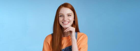 Stylish confident happy smart creative redhead girl look delighted thoughtful like interesting suggestion touch chin smiling approval friendly talking, standing blue background wear overalls photo
