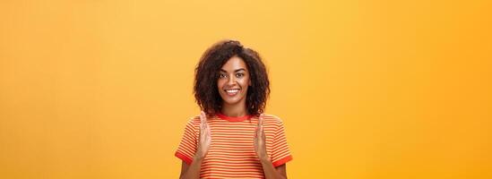 retrato de encantador de apariencia amistosa africano americano mujer con afro peinado explicando historia con manos y gestos formación objeto, participación palmas vertical terminado cofre y sonriente a cámara foto