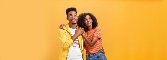 Couple of lovers enjoying spending warm summer evening together gazing up at stars with happy enthusiastic expression being in love hugging and expressing warm romantic feelings over orange wall photo