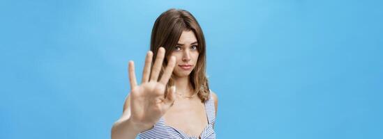 Silly and shy insecure attractive girl pulling hand towards to cover face from camera making moody timid expression asking to stop not liking what happening saying no with body language over blue wall photo