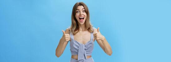 mujer satisfecho con Perfecto resultado sonriente emocionado con contento mueca demostración pulgares arriba gesto posando en elegante pareo cerrado terminado azul fondo, curioso emocionado y Encantado a cámara foto