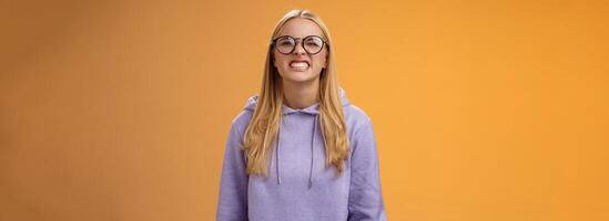 Blond girl show teeth warn can stand herself bite, fool around grimacing funny wearing purple hoodie glasses standing orange background better not mess with me, pranking friend have fun photo