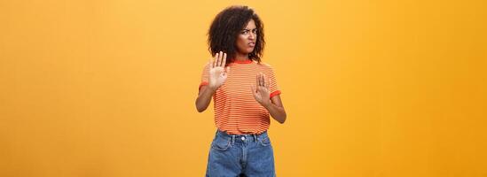 No I refuse. Intense suspicious and displeased smart african-american female rejecting bad offer pulling raised palms turning away with aversion and dissatisfied look against orange background photo