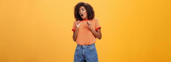 No do not hurt me. Scared silly and insecure good-looking african american woman in stupor screaming for help turning away raising palms near body in defence standing in fright over orange wall photo