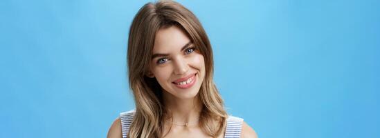 Waist-up shot of charming self-assured authentic woman feeling great accepting own imperfections tilting head smiling broadly at camera and showing cute gapped teeth posing over blue background photo