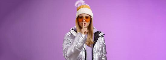 Sassy flirty gorgeous woman enjoying vacation snowy mountain resort wear winter hat silver stylish jacket sunglasses asking promise not tell secret show shush shhh gesture index finger seal lips photo