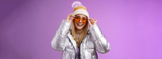 Good-looking charming happy smiling blond girlfriend having fun vacation girlfriends put on sunglasses grinning delighted wear cool silver glittering jacket warm winter hat, purple background photo