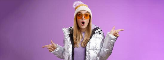 Impressed blond girl gasping widen eyes surprised folding lips wow sound check out incredible discounts winter equipment pointing left right cannot choose standing astonished purple background photo