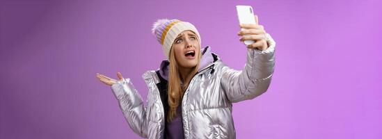 Upset bothered whining blond girl complaining cannot find right angle take selfie with cool sightseeing during vacation travelling abroad yelling smartphone pointing aside, purple background photo