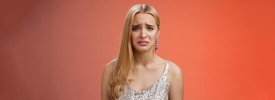 Disappointed complaining cute blond woman in silver stylish dress grimacing frowning upset have bad day pouting pity standing displeased unhappy heartbroken everything bad, red background photo