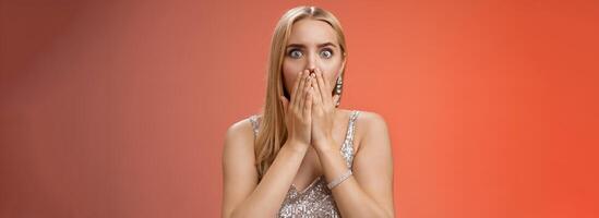 Concerned shocked worried blond woman terrified gasping cover mouth hands pray gesture widen eyes witness terrible accident worry expressing empathy pity, standing red background uneasy photo