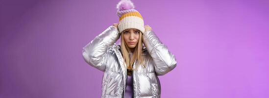 Upset gloomy complaining blond girlfriend whining standing upset disappointed sulking offended pulling hat forehead look offended unhappy wearing stylish glittering jacket unwilling go outside cold photo