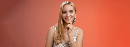 Close-up charming tender young cute blond girl in silver stylish party dress touching chin smiling friendly listen curiously interesting conversation standing red background amused, entertained photo