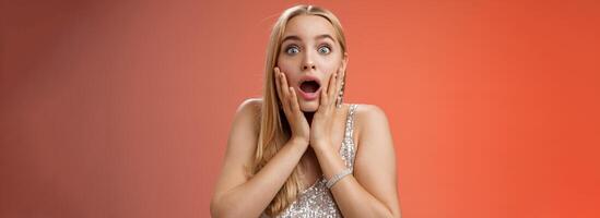 Shocked speechless concerned young stunned woman gasping screaming worried drop jaw touch cheeks widen eyes surprised nervously staring camera troubled afraid, standing red background photo