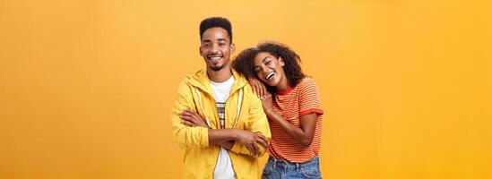 Awesome when boyfriend is best friend. Portrait of charming friendly african american woman leaning on guy touching his shoulder feeling happy they together and she can rely on posing orange wall photo