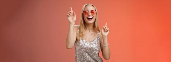 Amused attractive happy smiling woman dancing nightclub having fun enjoying go wild party celebrating b-day wearing stylish dress sunglasses raise index fingers smiling singing along photo