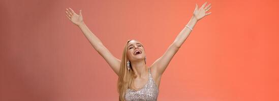 Waist-up carefree happy girl fulfill dream raising hands up sky joyfully close eyes smiling celebrating good perfect news triumphing achieve success victory, standing thrilled red background photo