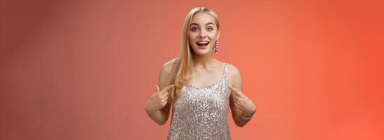 Surprised wondered happy blond charming cheerful woman in glittering silver dress pointing herself amused thrilled picked be chosen participate awesome event, standing joyful red background photo