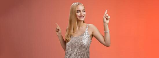 Carefree good-looking stylish glamour blond young 20s woman in silver glittering dress dancing having fun amused go wild party night prom shaking body raising index fingers up, red background photo