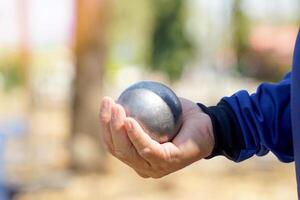 jugadores sostener un petanca pelota en su manos y preparar a lanzar eso en orden a sitio el petanca pelota como cerca a el objetivo pelota como posible. foto