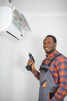 African American electrician repairing air conditioner indoors photo
