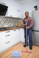 profesional limpiador en azul uniforme Lavado piso y limpiando polvo desde el mueble en el vivo habitación de el departamento. limpieza Servicio concepto foto