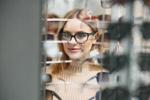 Pretty young woman is choosing new glasses at optics store. photo