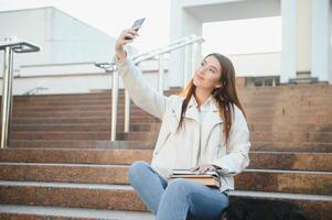 Female college student with books outdoors. Smiling school girl with books standing at campus. I'm prepared for exam very well. Portrait of perfect student at the university photo