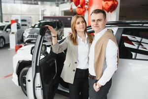 Happy young couple chooses and buying a new car for the family in the dealership photo