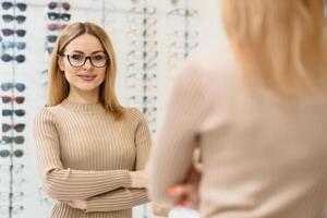 Pretty young woman is choosing new glasses at optics store. photo