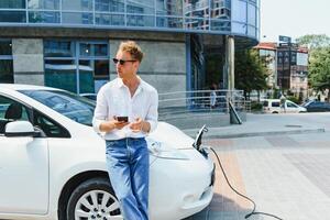 Handsome man using phone while car being charged photo