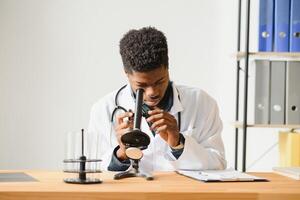 Portrait of young African-American man looking in microscope while working on medical research in laboratory, copy space. photo