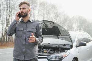 Man use a cellphone call garage in front of the open hood of a broken car on the road in the forest. Car breakdown concept. photo