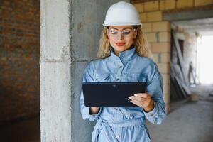 absorbido en el trabajo de un mujer ingeniero trabajando con un tableta en el antecedentes de el construcción sitio. retrato de un joven arquitecto, protector equipo. selectivo enfocar. foto