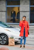 preguntándose acerca de nuevo tecnología. mujer en el eléctrico carros cargar estación a tiempo de día. foto