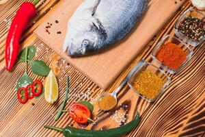 Fresh raw dorado fish. Sea bream, lying on a wooden board on a table with herbs and salt and spices. Dorado and ingredients for cooking on the table. Close-up photo