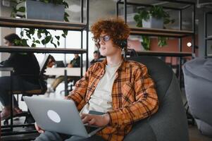 Portrait of cheerful millennial blogger with modern cellphone and laptop technology enjoying freelance lifestyle, happy hipster guy in optical eyewear using mobile phone and netbook in street cafe. photo