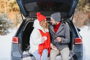 Smiling together. Nice couple have weekend at countryside at winter time. Sitting on the rear part of modern car. photo