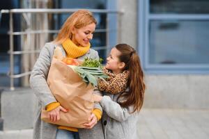 contento familia después compras con compras pantalones en estacionamiento cerca centro comercial. madre con hija. foto