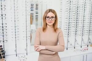 Pretty young woman is choosing new glasses at optics store. photo