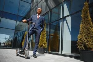 Handsome african 30s man wearing coat smiling while riding electric scooter outdoors photo