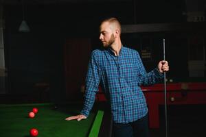 joven hermoso hombre propensión terminado el mesa mientras jugando snooker foto